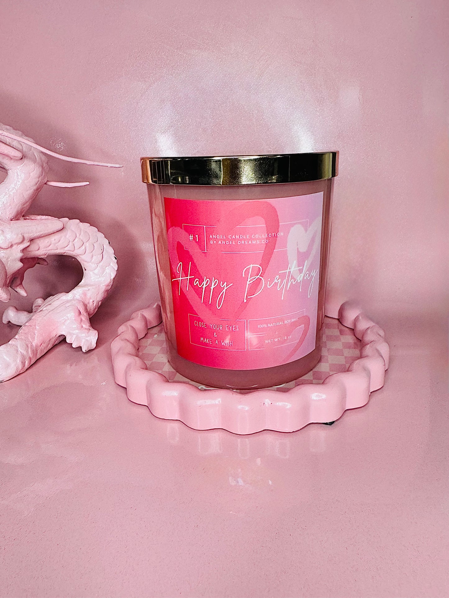 Pink candle with a gold lid on a pink stand against a pink background